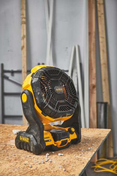 En bärbar sladdlös fläkt från DEWALT (modell DCE512B) står på en träarbetsbänk i en verkstad med byggmaterial i bakgrunden.